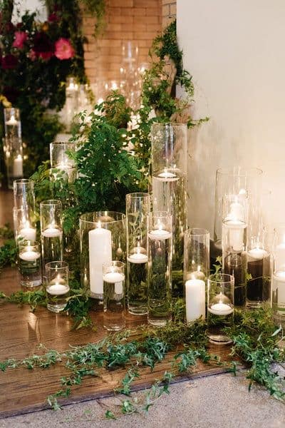 Tall glass vases with floating candles and greenery arranged on a wooden floor, creating a soft, ambient glow.