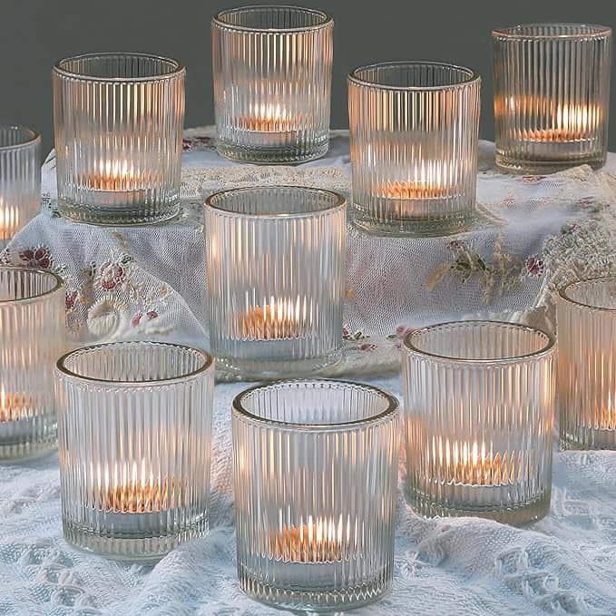 Several lit candles in ribbed glass holders arranged on lace fabric.